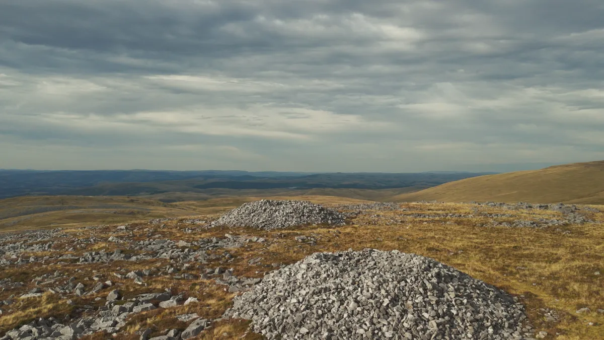 A large Bronze Age burial cairn of pale stones on the Garreg Las ridge under heavy cloud