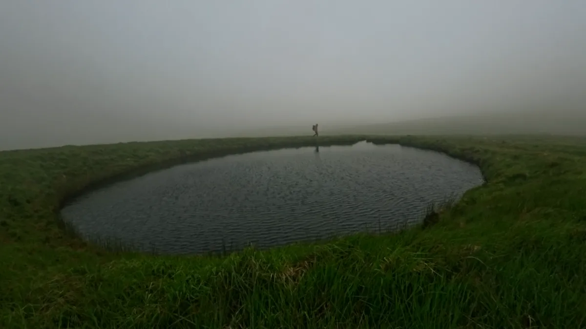 A pool in a large shakehole on the misty plateau with a lone walker on its far rim