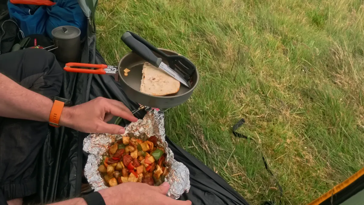 Chorizo and halloumi hash in a foil parcel, with a flatbread toasting in a frying pan on the stove behind