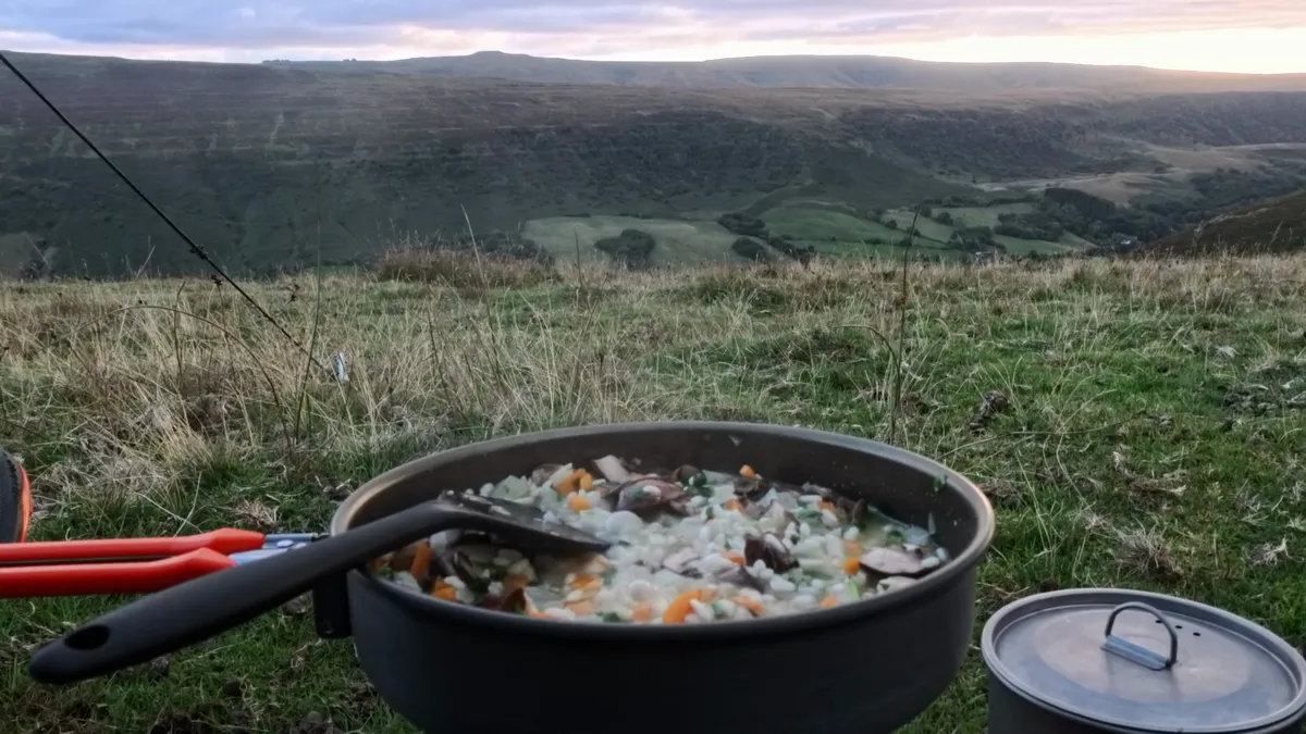 A frying pan of risotto and a lidded titanium pot on the grass, the Vale of Ewyas spread out below in evening light
