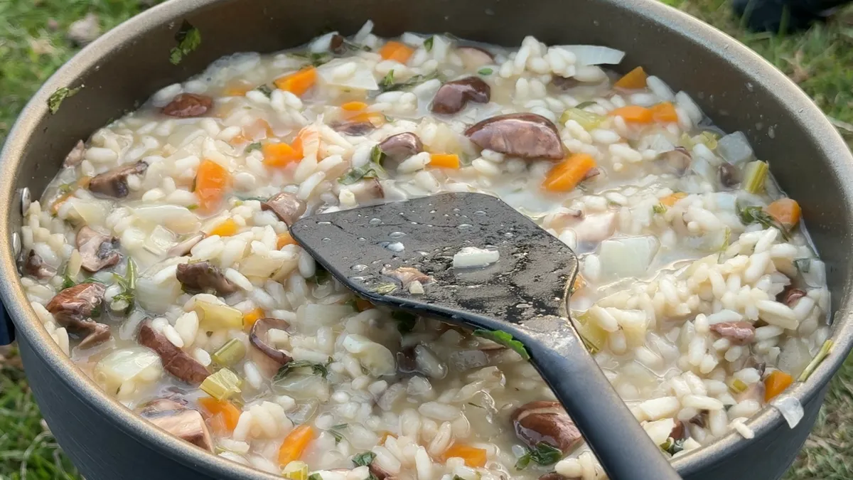 Close-up of mushroom risotto with carrot, onion and parsley in a frying pan, a black spatula resting in it
