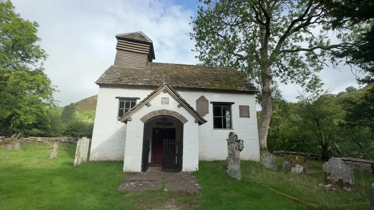 The small whitewashed chapel of St Mary at Capel-y-ffin, with a wooden bellcote, among gravestones and trees