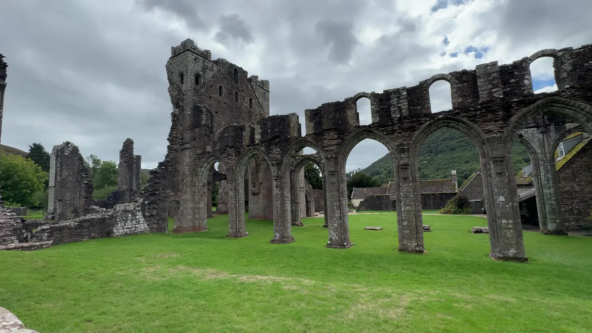 The ruined nave arcade of Llanthony Priory on a green lawn, the valley side rising behind